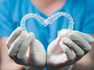 A dental professional s hands holding a transparent heart-shaped object, possibly representing dental implants or orthodontic devices.