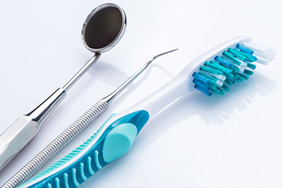 The image shows a collection of dental tools, including a toothbrush with blue bristles and a pair of scissors, placed on a white background.