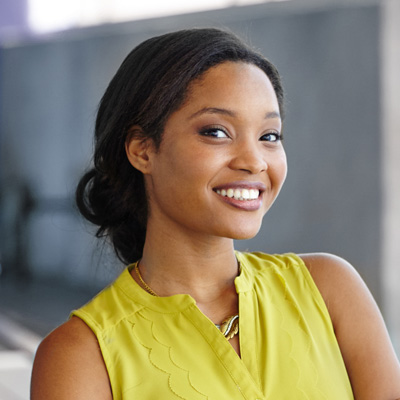 A young woman with a radiant smile, wearing a yellow top and posing against a blurred background.